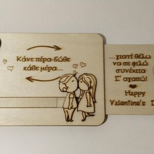 May include: A wooden Valentine's Day card with a sliding mechanism. The card features engraved text and illustrations of a couple, hearts, and arrows. The text includes "Happy Valentine's Day".