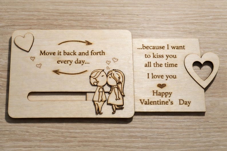 May include: A wooden Valentine's Day card with a kissing couple illustration. The card has a heart-shaped cutout and includes the phrases "Move it back and forth every day..." and "...because I want to kiss you all the time. I love you. Happy Valentine's Day."