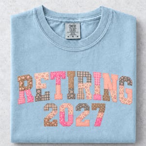 Może przedstawiać: Jasnoniebieska koszulka Comfort Colors z napisem "RETIRING" i numerem "2027" w stylu patchwork. Litery mają wzory kwiatowe i kratę w odcieniach różu, brązu i brzoskwini.