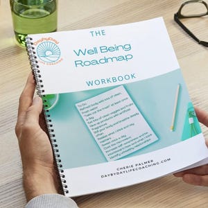 May include: A spiral-bound workbook titled "The Well Being Roadmap." The cover features a teal and white design with the text "WORKBOOK." The workbook is open, revealing a list of "To Do" items. A pencil and glasses are visible.