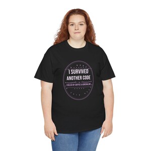 Puede incluir: Una camiseta negra de manga corta con un gráfico circular blanco y morado claro en el pecho. El texto dentro del círculo dice I SURVIVED ANOTHER CODE y FUELED BY COFFEE & ADRENALINE, rodeado de líneas decorativas y pequeñas estrellas.