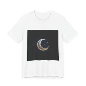 Puede incluir: Camiseta blanca con un diseño gráfico cuadrado oscuro. El diseño muestra una luna creciente dorada y plateada, rodeada de estrellas sobre un fondo negro. El texto "Celestial Night Forms" está debajo de la luna.