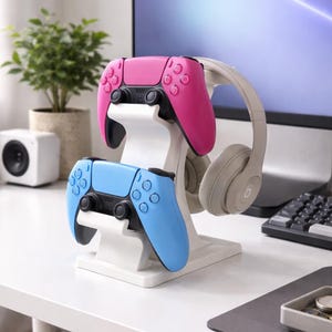 May include: A white gaming controller stand holding a pink and a blue controller, with a pair of grey headphones. The controllers have black accents and buttons. The stand is on a white desk.
