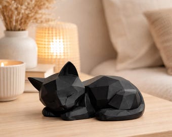 Peut inclure: Une sculpture de chat géométrique noire en position de sommeil. La figurine de chat est faite de multiples surfaces planes, créant un design à facettes. Le chat est posé sur une surface en bois de couleur claire.