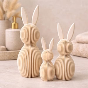 Pode incluir: Três estatuetas de coelho de madeira em tamanhos variados. Os coelhos têm um design canelado e em camadas e orelhas longas e verticais. A cor é bege claro natural. Os coelhos são um item decorativo, perfeito para a Páscoa ou a primavera.