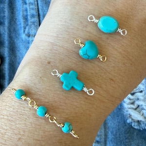May include: Turquoise gemstone charms in various shapes, including an oval, heart, and cross, are displayed. The charms are wire-wrapped with gold and silver-colored wire. A bracelet with turquoise beads and gold wire is also shown.