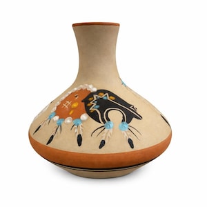 May include: Tan ceramic vase with a narrow neck and rounded body. The vase features Native American-inspired designs in black, orange, and blue, with feather and bead motifs. A brown band encircles the base and rim.