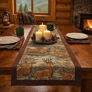 May include: A dining table set with a deer-themed table runner with brown borders. The table is set with plates, mugs, and candles. A fireplace and window with a forest view are in the background, creating a cosy, cabin-like atmosphere.