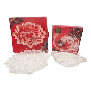 May include: Two clear glass serving dishes with a Christmas theme, one with a snowflake design and the other with a winter scene. Both are displayed with their original red boxes.