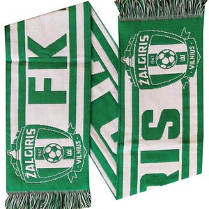 May include: A green and white knit scarf featuring the FK Zalgiris Vilnius soccer club logo, which includes a central soccer ball, the year 1947, and the text Zalgiris Vilnius. The scarf has fringed ends and large green letters spelling FK Zalgiris.