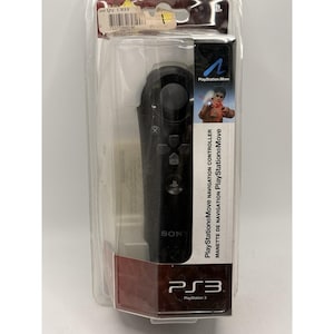 May include: A black PlayStation Move navigation controller in its original packaging. The controller has several buttons and a joystick. The packaging includes the PlayStation 3 logo and the text "PlayStation Move Navigation Controller".