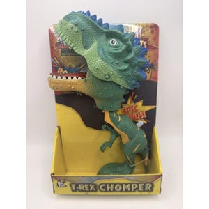May include: A green and yellow T-Rex Chomper toy in its original packaging. The dinosaur toy has a detailed head and body, with blue accents on its head. The packaging is yellow and black with the text "EPIC FUN!" and "T-REX CHOMPER".