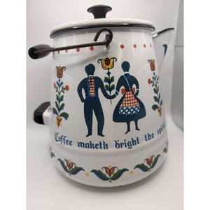 May include: White enamel coffee pot with a black handle and lid. The pot features a folk art design of a couple holding hands, floral accents, and the text "Coffee maketh bright the spirit."