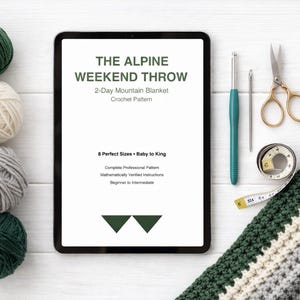 Digital crochet pattern displayed on tablet with yarn balls, scissors, and crochet supplies on white wooden background
