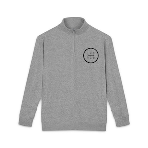 May include: A grey long-sleeved sweatshirt with a quarter-zip collar. A black circle graphic on the left chest shows a gear shift pattern with the numbers 1, 3, 5, 2, 4, and R. The sweatshirt is made of a soft, comfortable material.