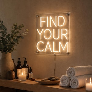 May include: A square, clear acrylic neon sign featuring the warm white illuminated text "FIND YOUR CALM" in a sans-serif font. The sign is mounted with four silver hardware standoffs and includes a thin power cord extending from the bottom edge.
