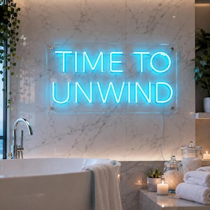 May include: A rectangular clear acrylic sign featuring bright blue neon lettering that reads TIME TO UNWIND. The sign is mounted on a white marble wall above a bathtub, with four silver metal standoffs securing the corners of the acrylic panel.