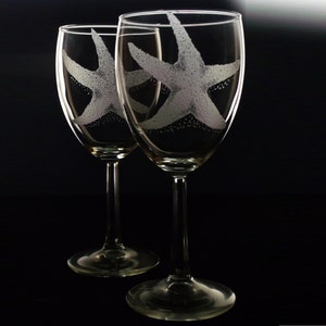 Peut inclure: Deux verres &agrave; vin transparents avec des motifs d'&eacute;toiles de mer grav&eacute;s. Les verres sont sur un fond noir.