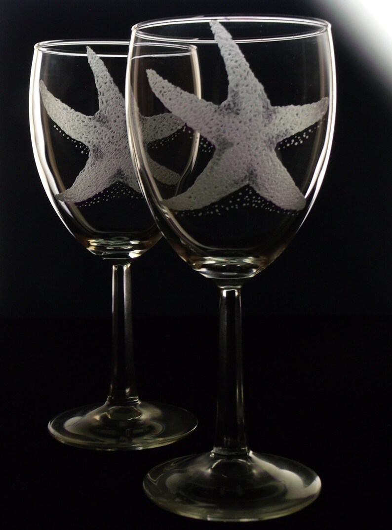 Peut inclure: Deux verres &agrave; vin en verre transparent avec des &eacute;toiles de mer blanches grav&eacute;es. Les verres sont sur un fond noir.