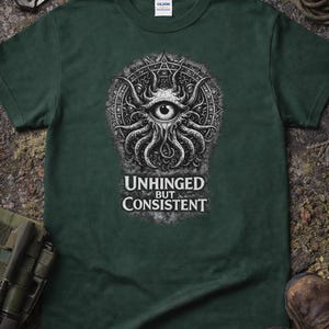 Könnte beinhalten: Dunkelgrünes T-Shirt mit einem schwarz-weißen Grafikdesign eines Auges, umgeben von Tentakeln und einem kreisförmigen Design. Der Text "UNHINGED BUT CONSISTENT" steht darunter. Das T-Shirt ist aus weichem Material.