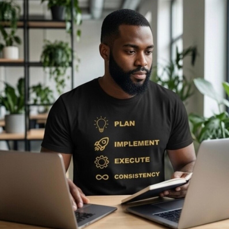 K&ouml;nnte beinhalten: Ein schwarzes Kurzarm-T-Shirt mit goldfarbenen Grafiken und Text. Das Design zeigt ein Gl&uuml;hbirnen-Symbol mit dem Wort PLAN, eine Rakete mit IMPLEMENT, ein Zahnrad mit EXECUTE und ein Unendlichkeitssymbol mit dem Wort CONSISTENCY.
