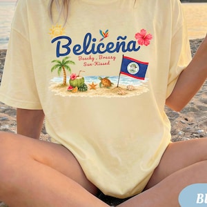 Pode incluir: Uma t-shirt amarelo-claro com uma estampa gráfica contendo o texto "Beliceña" e "Beachy, Breasy, Sun-Kissed". O design inclui uma palmeira, um coco, uma tartaruga marinha, uma flor de hibisco, um papagaio e a bandeira do Belize.