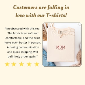 May include: Cream-colored t-shirt with the word "MOM" in burgundy, and "EST.2026" below it. The shirt is folded, with a necklace draped over it. The image includes customer reviews and the text "Customers are falling in love with our T-shirts!"