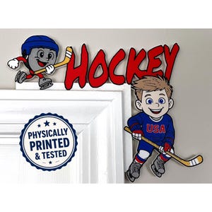 May include: A decorative wooden door corner sign featuring the red text HOCKEY, a cartoon hockey puck character wearing a blue helmet and skates, and a cartoon hockey player in a blue USA jersey holding a hockey stick, with a circular seal.