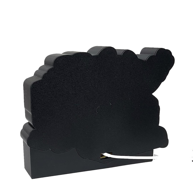 Puede incluir: Una luz decorativa negra con forma de nube con una superficie similar al fieltro. La luz tiene una base rectangular y un cable blanco que se extiende desde la parte inferior. La parte superior de la luz tiene un dise&ntilde;o ondulado en forma de nube.