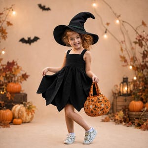 May include: A black witch hat with a green band and a black sleeveless dress with a petal-shaped hemline. The outfit is paired with a round orange fabric trick-or-treat bag featuring a pattern of ghosts, bats, and pumpkins, and white sneakers.