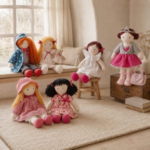 May include: A collection of seven fabric dolls with embroidered facial features and yarn hair. The dolls wear various outfits including dresses, a hooded jacket, and a tiara, with one doll holding a small teddy bear and another holding a star wand.