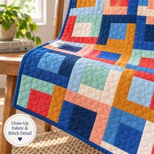 May include: A quilt featuring a geometric pattern of squares in shades of navy blue, bright red, mustard yellow, light mint green, and soft peach. The fabric has a visible quilted texture with a repeating stitch pattern throughout the surface.
