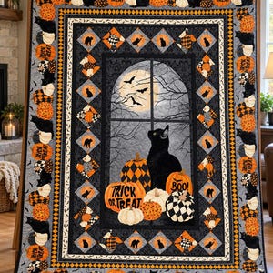 Könnte beinhalten: Ein rechteckiger Quilt mit einem zentralen Motiv eines schwarzen Katers vor einem Fenster mit Vollmond und Fledermäusen. Der Rand zeigt Kürbisse, schwarze Katzen sowie den Schriftzug "TRICK OR TREAT" und "BOO!" in Orange, Schwarz und Weiß.