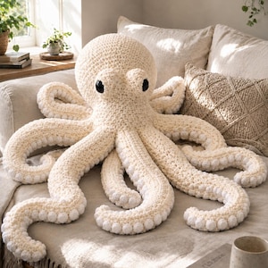 May include: A large, cream-coloured crochet octopus plush toy featuring a rounded head, two prominent black eyes, and eight long, curling tentacles. Each tentacle is adorned with a series of small, white, circular textured suckers along the underside.