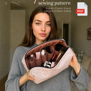 Op de afbeelding: Een doorgestikt lichtroze make-uptas naaipatroon in PDF-formaat. De tas heeft een gouden rits en interne verdelers voor organisatie. De afmetingen zijn 31 cm breed, 17 cm hoog en 11 cm diep. De tekst op de afbeelding luidt Makeup pouch sewing pattern.