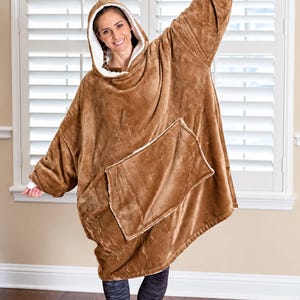 May include: An oversized brown hooded sweatshirt with a plush texture, featuring a large front pocket and a white fleece-lined interior. The garment includes long sleeves with white cuffs and a hood, providing a loose and comfortable fit.