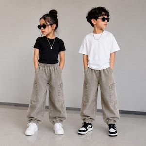 Puede incluir: Dos niños con ropa informal. Uno lleva una camiseta negra, un collar plateado y pantalones cargo de color marrón claro con zapatillas blancas. El otro lleva una camiseta blanca, un collar plateado y pantalones cargo de color marrón claro con zapatillas negras y blancas.