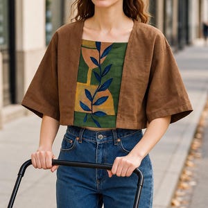 May include: A brown cropped jacket with wide sleeves worn over a square-neck top featuring a green background, yellow geometric shapes, and a dark blue leaf pattern, paired with blue denim jeans.