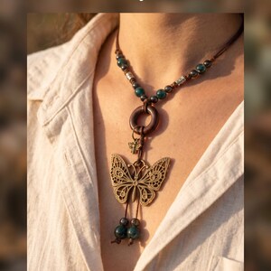 May include: A necklace featuring a large bronze-toned butterfly pendant, a small bee charm, and a dark wooden ring on a brown cord. The design includes dark green and metallic beads, with the text "Earthy, wild, and free. Your new favorite." and "HANDCRAFTED JEWELRY" visible.