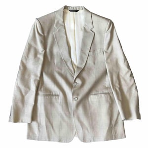 May include: A light beige blazer with a subtle plaid pattern. The jacket features a notched lapel, two front pockets, and two buttons for closure. The interior lining is a lighter shade of beige.