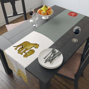 Può includere: Runner da tavolo con un design bianco e grigio. La sezione bianca presenta un'illustrazione di ghepardo. La sezione grigia ha un motivo a onde e un quadrato rosso con un carattere giapponese. Un piatto con forchette e una ciotola di mele sono sul tavolo.