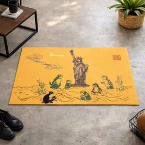 May include: A rectangular yellow floor mat featuring a dark blue illustration of the Statue of Liberty surrounded by various frogs and rabbits in a stylized sea. The text 1996 ANCHOR FEAST is printed near the top left, with a red square seal.