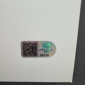 May include: A holographic sticker with a QR code and the number 56245. The sticker has a design of a green and blue image. The sticker is on a white surface.