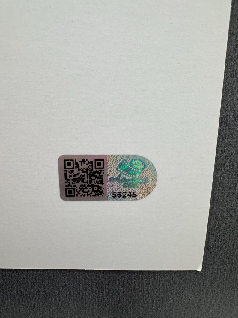 May include: A holographic sticker with a QR code and the number 56245. The sticker has a design of a green and blue image. The sticker is on a white surface.