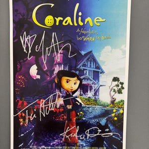 May include: A Coraline movie poster with a purple and blue background. The title "Coraline" is in yellow, with the tagline "An Adventure too Weird for Words." The poster features the character Coraline and several signatures.