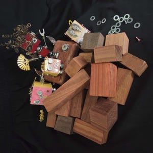 May include: An assortment of wooden blocks in various sizes and shapes, alongside several steampunk-inspired art pieces. The art pieces feature metallic accents, wings, and decorative elements. The background is a solid black.