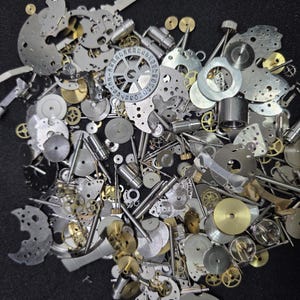 May include: A collection of disassembled watch parts, including gears, plates, and screws, in various metallic finishes. The components are scattered across a dark surface, showcasing the intricate details of watch mechanisms.