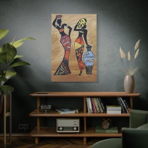 May include: An abstract painting of two figures in long dresses with geometric patterns. One figure carries a basket on their head, the other leans on a blue vase. The artwork is set against a tan background.
