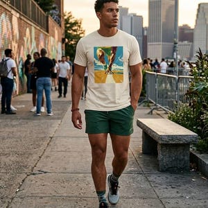 May include: A person wearing a cream-colored t-shirt with a graphic print, green shorts, and athletic shoes. The graphic on the shirt depicts a runner. The person is walking on a sidewalk with a brick wall and buildings in the background.