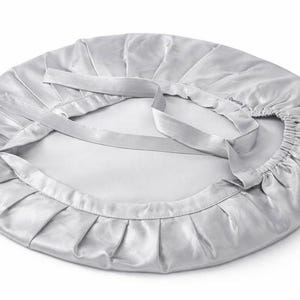 K&ouml;nnte beinhalten: Eine silberne Satinhaube mit ger&uuml;schtem Rand und zwei langen, flachen B&auml;ndern. Die Haube ist kreisf&ouml;rmig und scheint aus einem weichen, gl&auml;nzenden Material zu bestehen. Die B&auml;nder sind zum Binden konzipiert, um die Haube zu sichern.